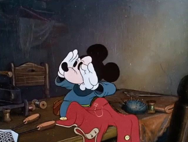 a cartoon of mickey mouse sitting at a table covering his eyes with his hands