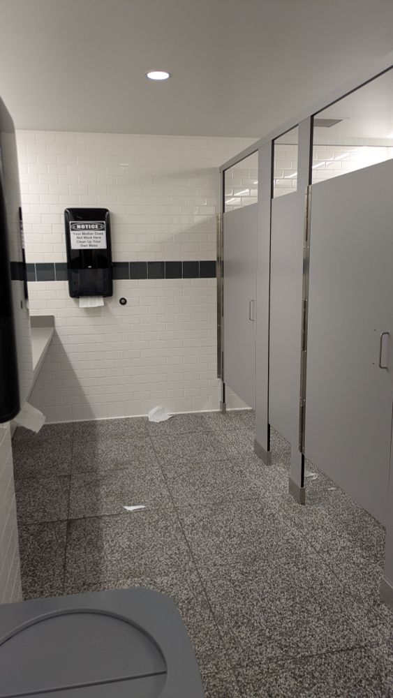 A few pieces of torn paper towel and toilet paper litter the floor of a men's restroom.