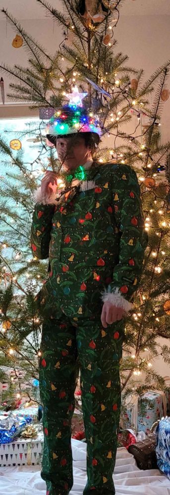 A goofy looking guy in a light up Christmas tree formal suit with RGB bowtie, and bowler hat that looks like the top of a Christmas tree.