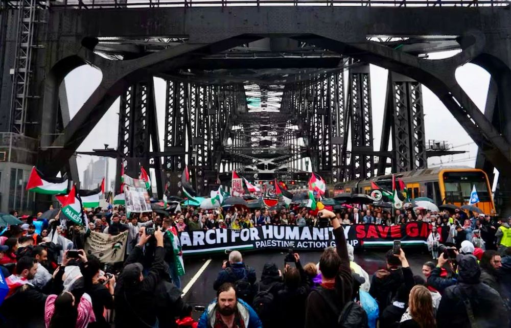 A photo of the March for humanity on the Sydney Harbour Bridge on August 3rd 2025. There is a large crowd of people walking on the bridge holding Palestinian Flags, Lebanese Flags, Watermelons. There is a large banner which says “March for Humanity. Free Gaza” Palestine Action Group.”

There are people gathered covering the entire length of the bridge. Many people are wearing Keffiyehs, a traditional Middle Eastern headdress, typically a square cloth, often made of cotton, that is worn by people in arid regions to protect from sun, dust, and sand. It's commonly found in the Levant (including Palestine, Jordan, Syria, and Lebanon) and other parts of the Middle East, where it's known by various regional names like shemagh or ghutra. Beyond its practical uses, the keffiyeh has become a powerful cultural and political symbol, particularly associated with Palestinian identity and resistance. 

The March, organised by the Palestine Action Group was banned by the Zionist premier of NSW Christopher John Minns, who was humiliated publicly by the Supreme Court who allowed the march to go ahead. 

The Police Force NSW also tried their hardest to stop the March, even closing the Harbour Bridge during the March. 

This protest focused on a variety of issues related to the conflict, including demands for a ceasefire, an end to the Israeli blockade, occupation and genocide,  protesting IDF war crimes, ending Australian support for Israel military and providing humanitarian aid to Gaza.

The Australian Prime Minister Anthony Albanese and Penny Wong were both mocked and derided constantly during the March for their inaction & doing nothing but show unbridled support for Tel Aviv in its extermination drive, and they’re both lied about arms to Israel.


