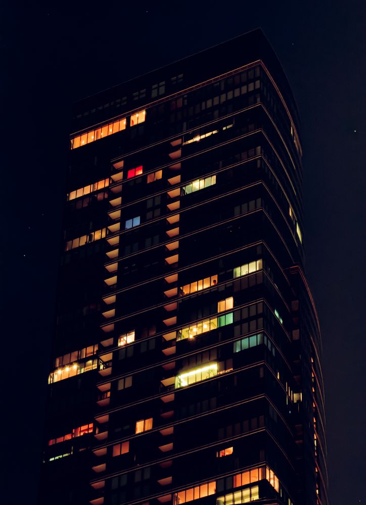 a dark, imposing building that rises far above you into a night sky that fades from a deep blue to a deeper one. the sentinel is littered with glowing windows of mostly orange. a few red, green, and blue windows pop.