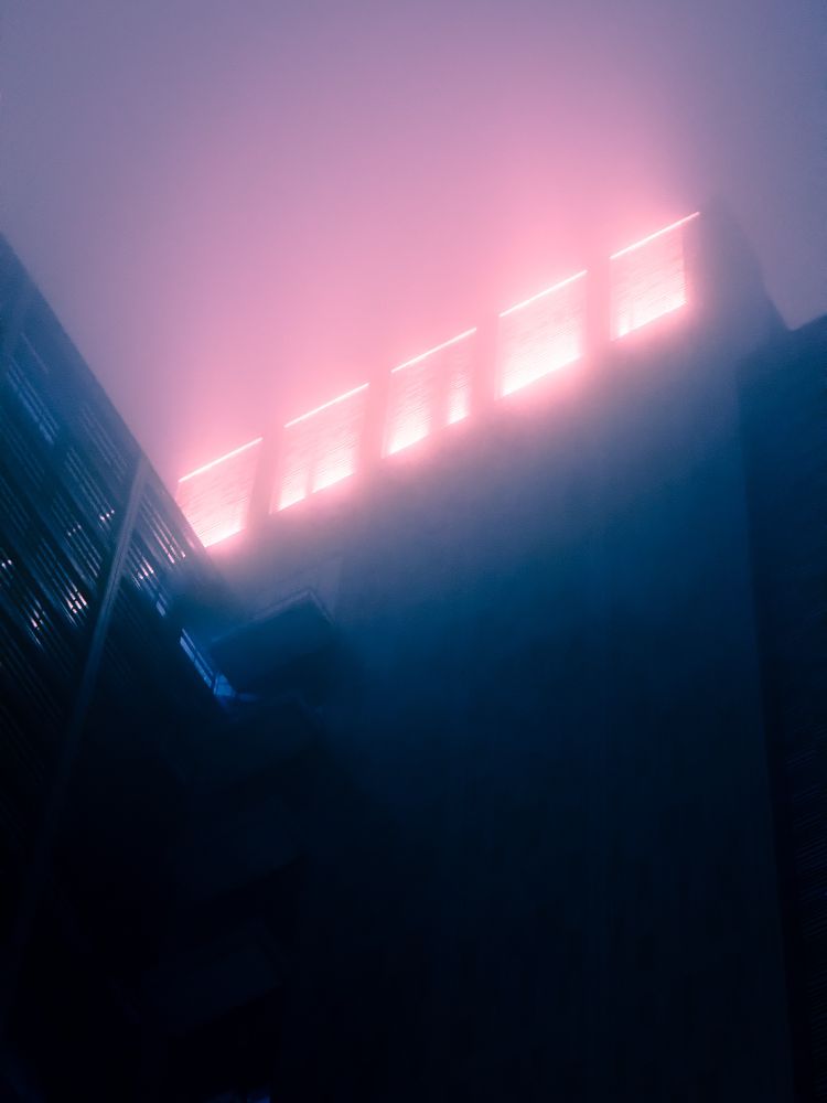 looking up at the top of a tall, dark building at night. the intense purple glow coming from the windows at the peak is, somehow, lonely.