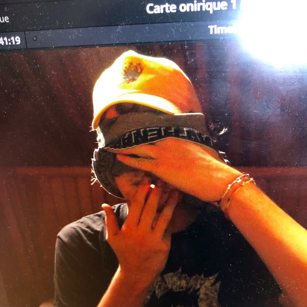 Photo de quelqu’un à casquette jaune qui soulève son masque gris pour fumer une clope 