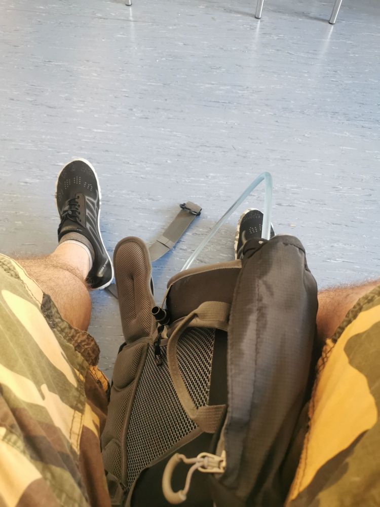Zu sehen sind zwei behaarte beine in einer kurzen camouflage hose, von oben fotografiert, Rucksack zwischen den Beinen.