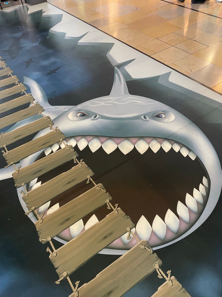 A painted shark under a painted rope ladder. This is on the floor of a shopping centre in Leith, Edinburgh. The shark has its mouth open wide, and if someone was dangling his legs over the side of the rope ladder, well, we know what would happen.

This is Sprizzy, I will not take questions on this one