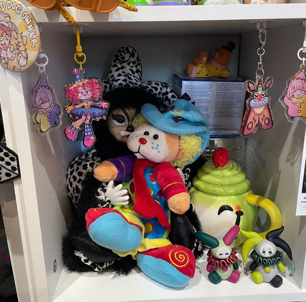 A cube shelf decorated with numerous jester and clown trinkets of sorts. Behind the clowns are boxes and a tin for my testosterone HRT injections. 