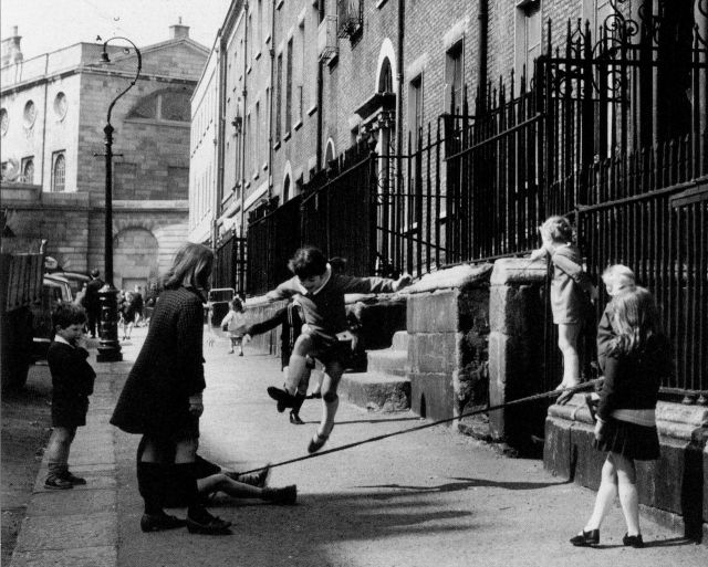 Black and white photo of children playing, jumping over a rope, on Henrietta Street in Dublin. 