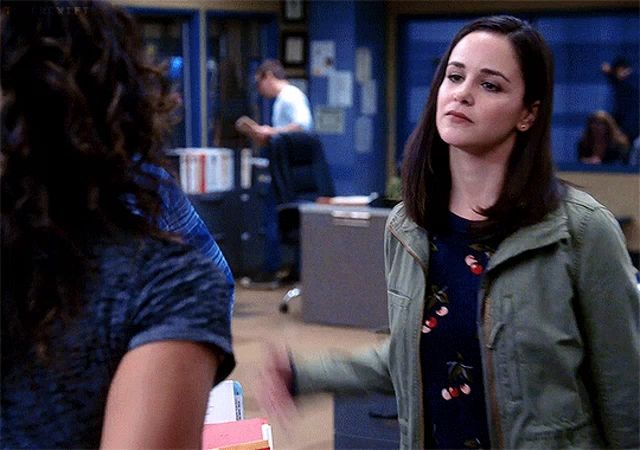 a woman in a blue shirt and a green jacket is talking to another woman