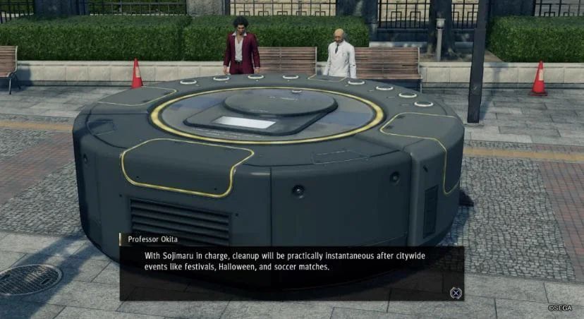 Capture d'écran du jeu Yakuza Like a Dragon.
Le héros et un vieux professeur sont dans la rue face à un roomba d'environ 3m de diamètre et 1m de haut.
Un encart de dialogue est ouvert en bas de l'écran.
Texte : "Professor Okita
With Sojimaru in charge, cleanup will be pratically instantaneous after citywide events like festivals, Halloween, and soccere matches."