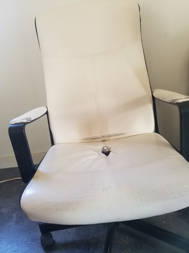 Un fauteuil de bureau blanc un peu usé, au centre de l'assise émerge le vérin métallique censé rester sous le fauteuil.