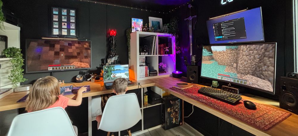 Three computers arranged on an L shaped desk. There is Minecraft on each screen. Two young girls are playing in two of the machines.