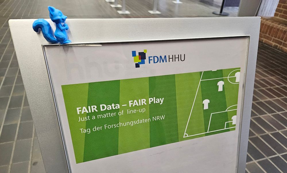 Ein Aufsteller mit einem Wegweiser zum Veranstaltungsort des Tages der Forschungsdaten in der ULB. Das Eichhörnchen von fdm.nrw sitzt oben drauf.