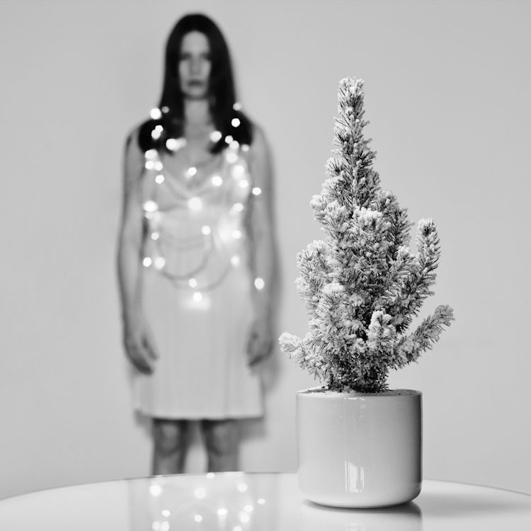 Konzeptuelles weihnachtliches Selbstportrait mit funkelnder Lichterkette als Halsschmuck und Tannenbaum im Vordergrund