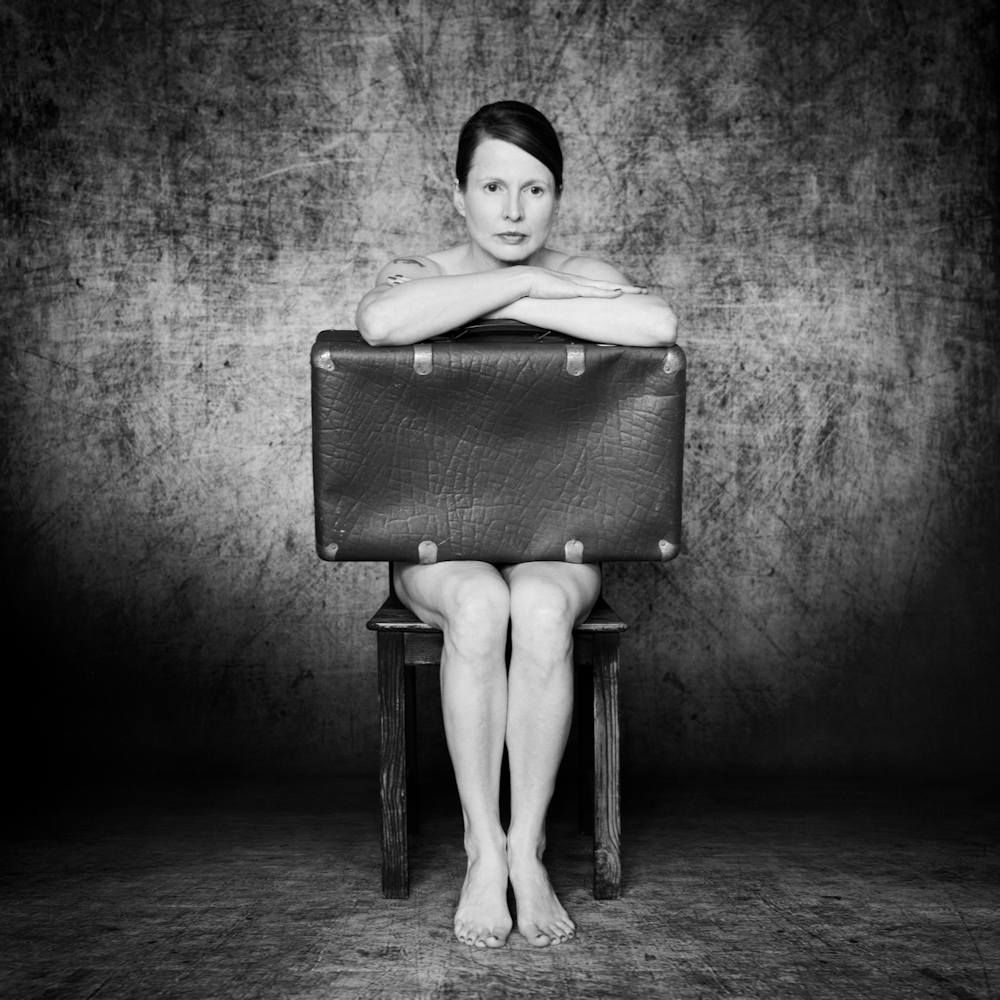 Schwarzweißes analoges Selbstportrait, mittig auf einem Stuhl sitzend mit einem alten Koffer auf dem Schoß