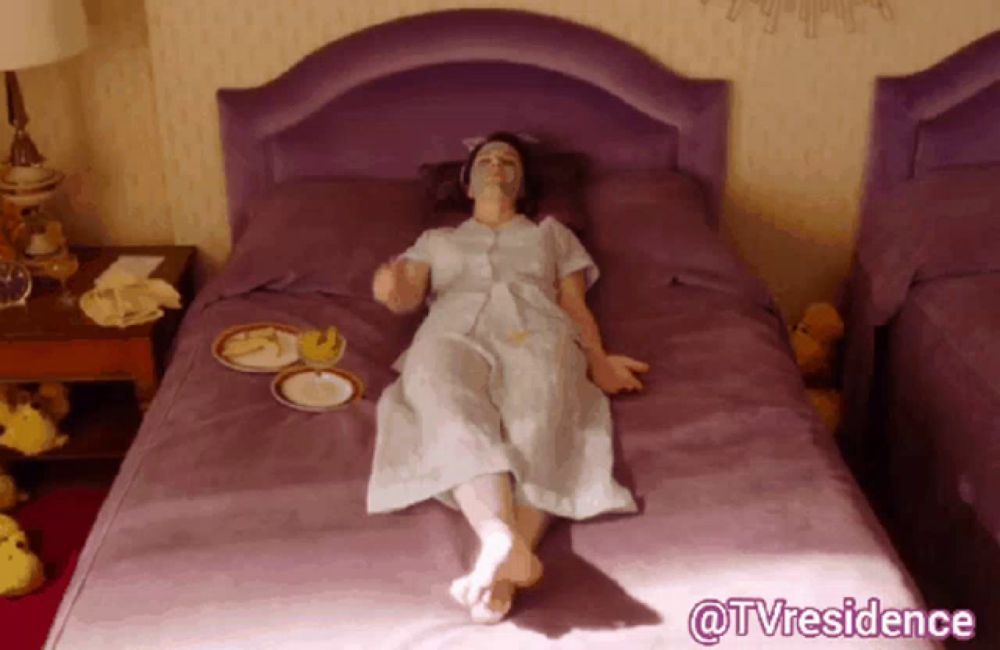 a woman is laying on a purple bed with a plate of food on the bed