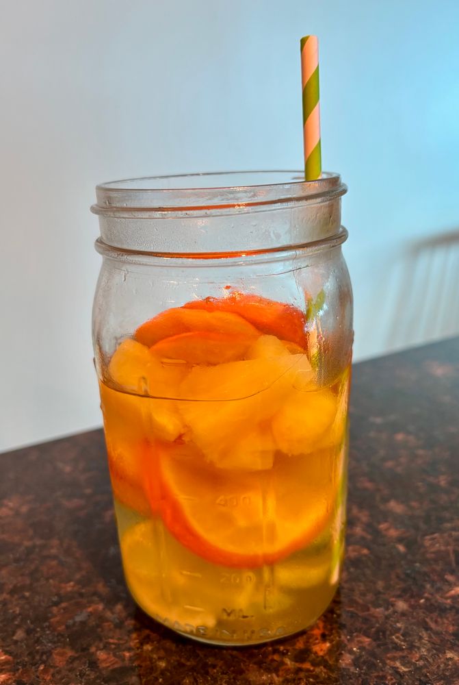 A mason jar of water infused with limes, oranges, and pineapple. 