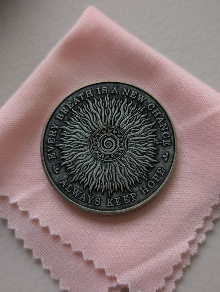 A reminder coin with the words "every breath is a new chance / always keep hope" sits on a pink cloth