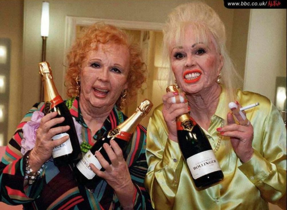Eddie and Patsy from Absolutely Fabulous (BBC), made up to look like senior citizens, wearing brightly coloured shiny clothing, smiling and holding bottles of champagne. Patsy is also holding a cigarette 