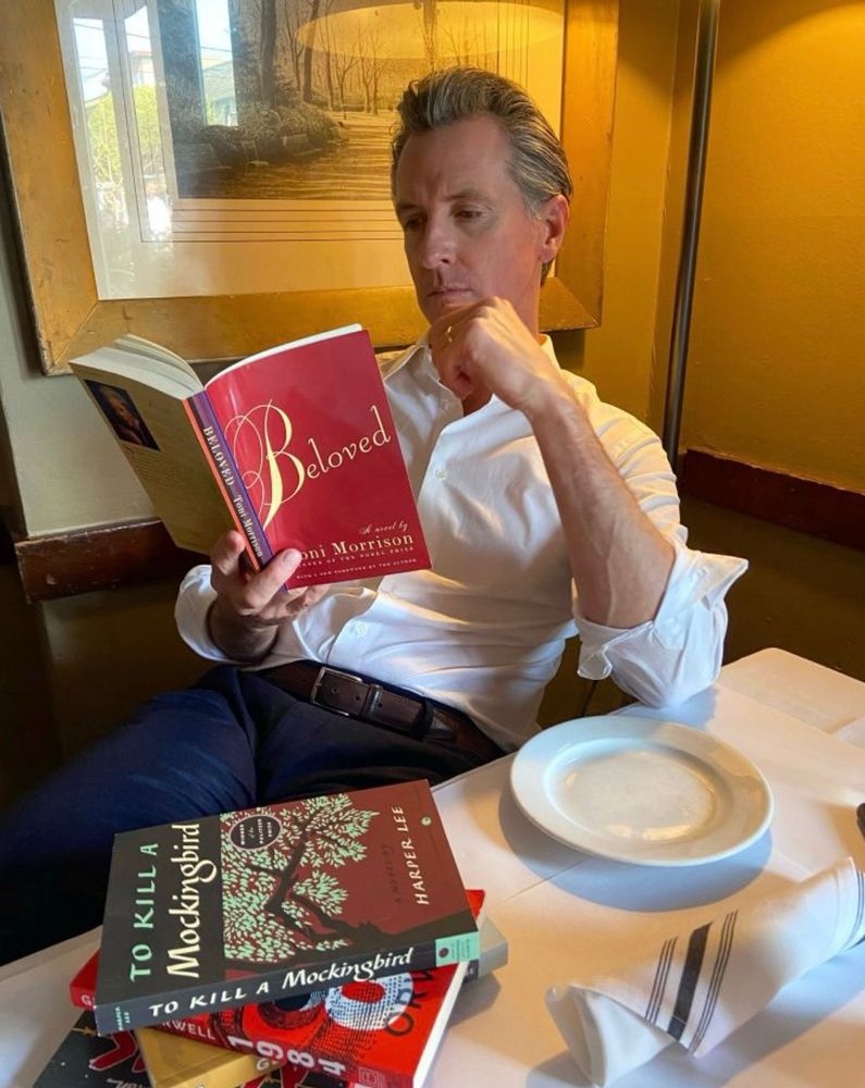 A study in cringe: a smug. over-gelled Gavin Newsom pretends to read Toni Morrison’s Beloved for the camera