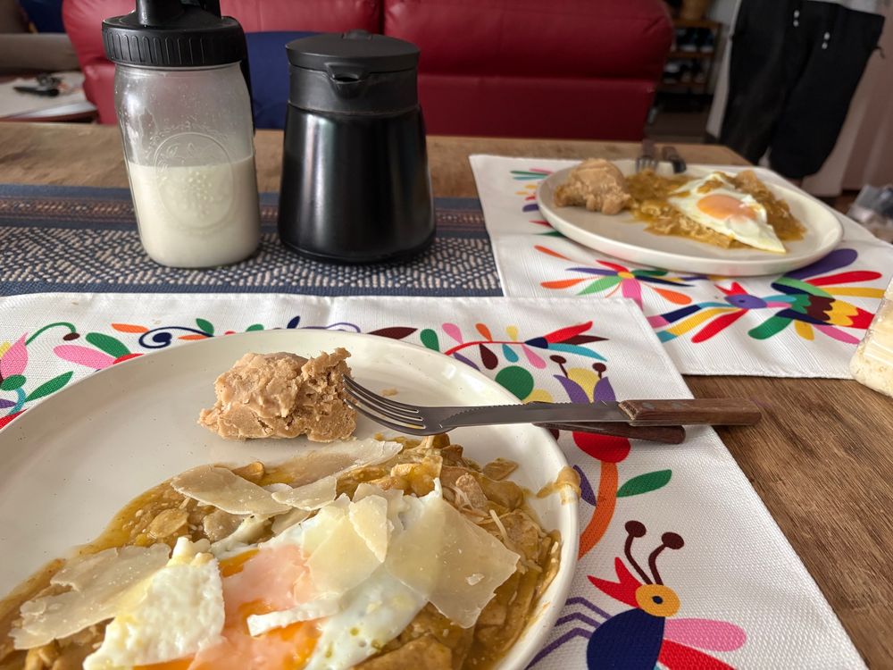 Dos platos sobre una mesa colorida de chilaquiles con huevo y frijoles refritos.