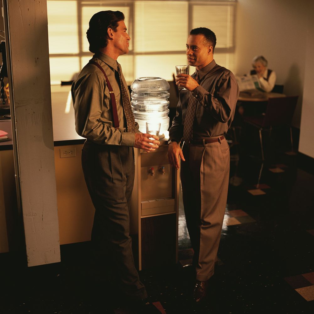 Two dudes standing around a watercooler, presumably having a 'watercooler conversation' about last night's Seinfeld or whatever.