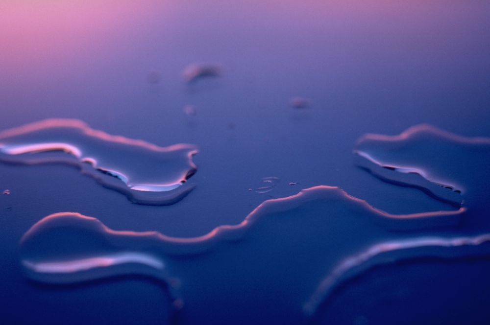 Water on a glass surface lit by hazy blue and purple light.
