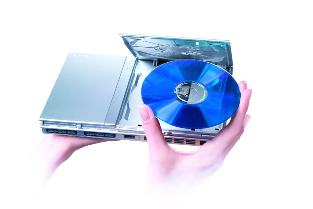 Someone putting a disc inside a satin silver PS2 slim.
