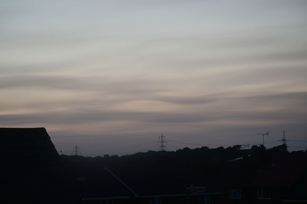 Wavy clouds in the sky in the evening with a house, pylons and trees also visible in the photo