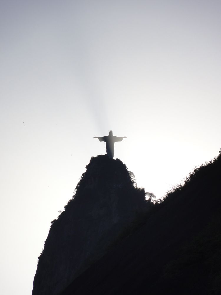 Foto do Cristo Redentor do Rio de Janeiro com a luz do sol batendo em uma névoa ao redor dele, gerando um belo efeito visual