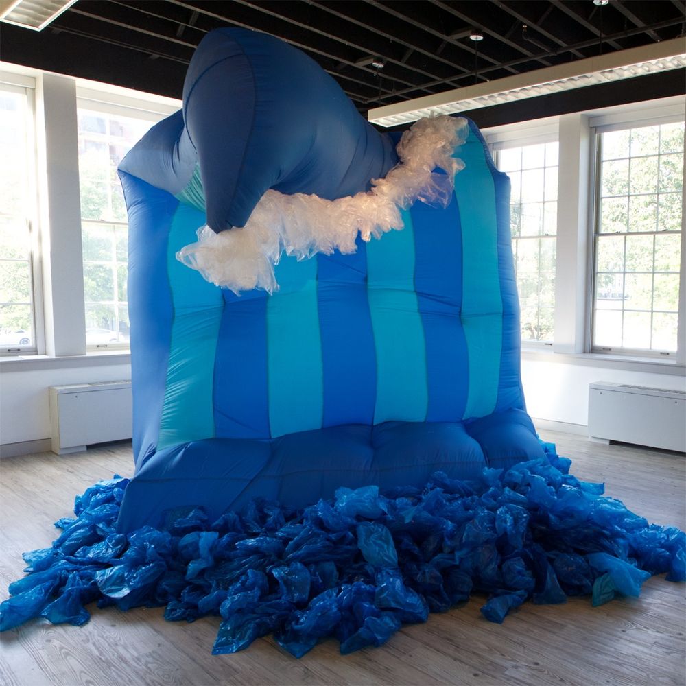 An inflatable blue soft sculpture made of nylon and woven shopping bags in front of a row of windows.