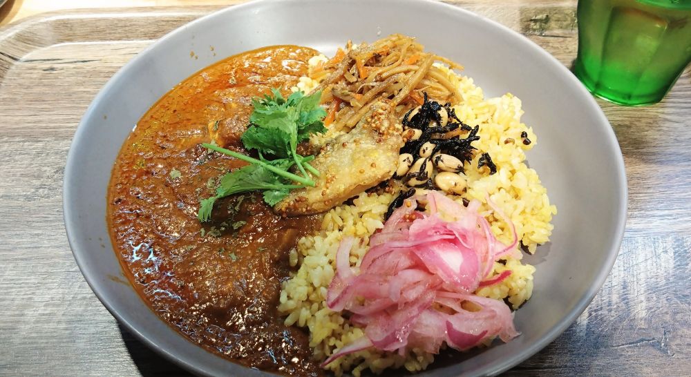 鯖カレー。きんぴらごぼうとかスパイスひじき豆とか、玉ねぎのアチャールとかパクチーが乗っている。