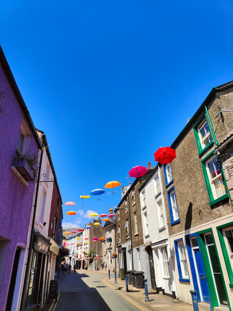  Colourful umbrellas are strung over a narrow, old fashioned street. The sky is the bluest blue