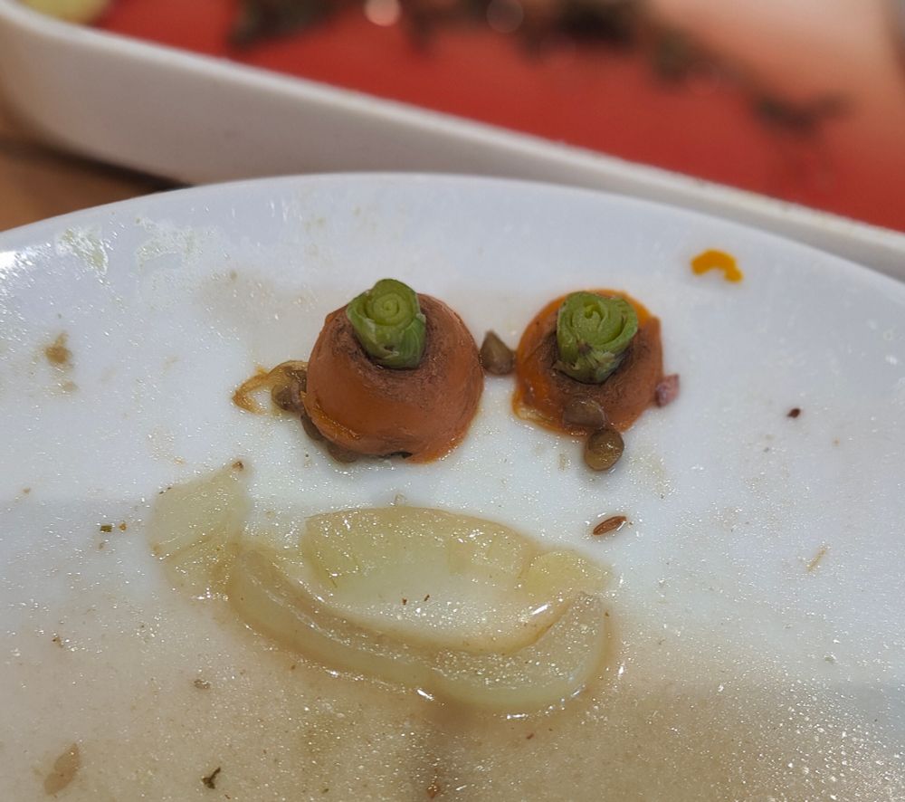 The tops of two carrots look like eyes at the top of a plate. Below, two slices of onion form a mouth