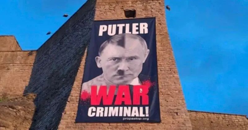 A poster on what looks like a castle wall, containing a composite photo of Putin and Hitler and the words "PUTLER WAR CRIMINAL!"