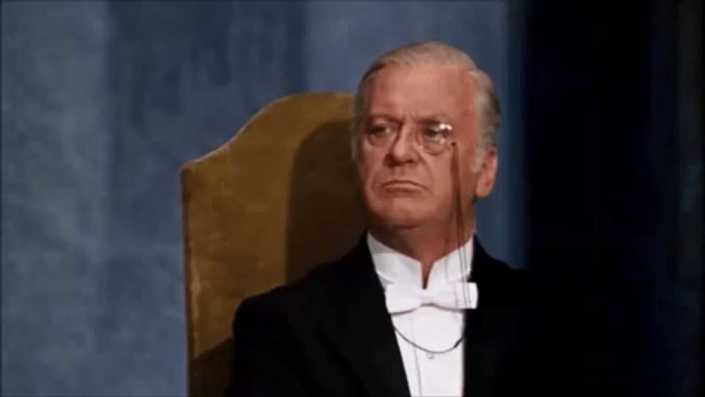 a man in a tuxedo and bow tie is sitting in a chair with his eyes closed