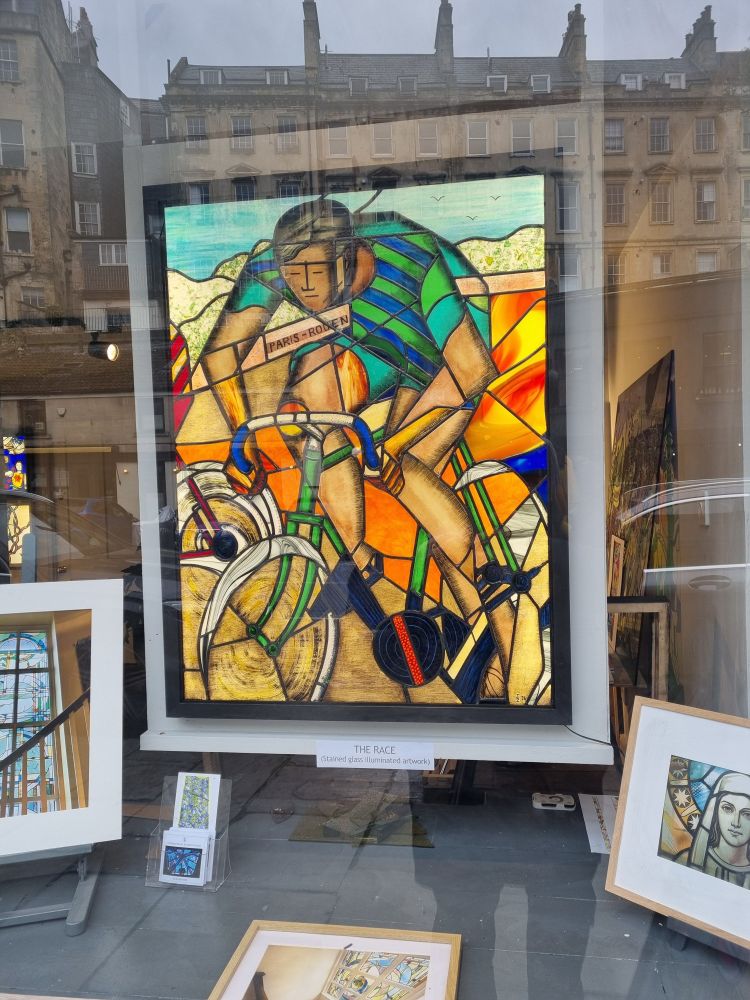 Framed artwork in stained glass of a male road cyclist, featured in the front window of a shop 