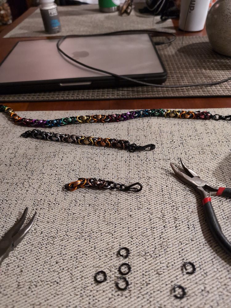 A long rainbow chain, a bear pride bracelet, and a partially complete bear pride chain, along with a pair of pliers 