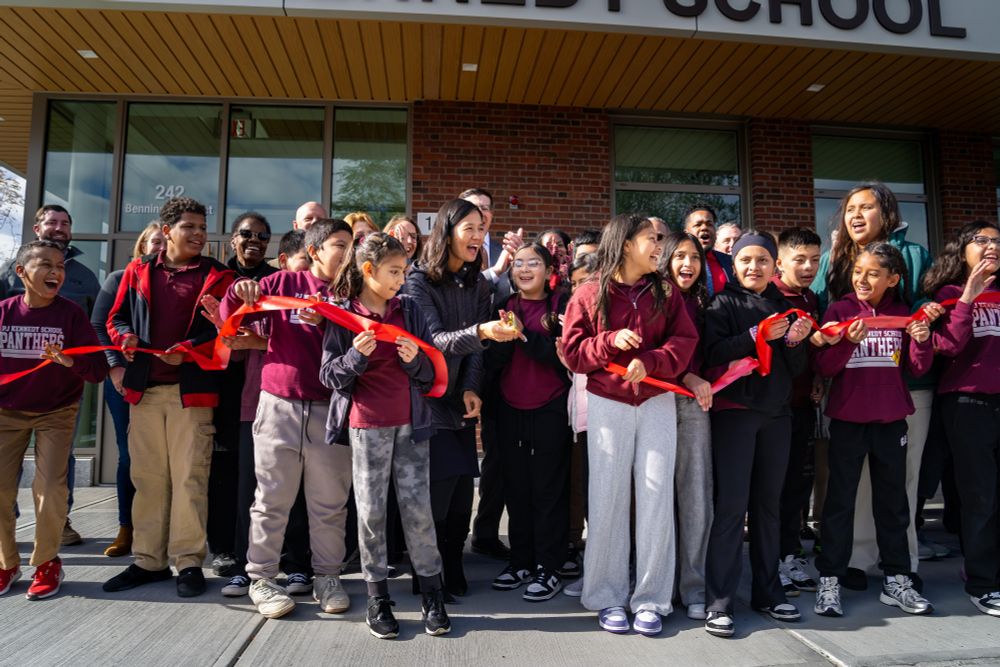 A large group of Boston Public Schools students and Boston Mayor Michelle Wu cut a red ribbon outside of the Kennedy Elementary School.  