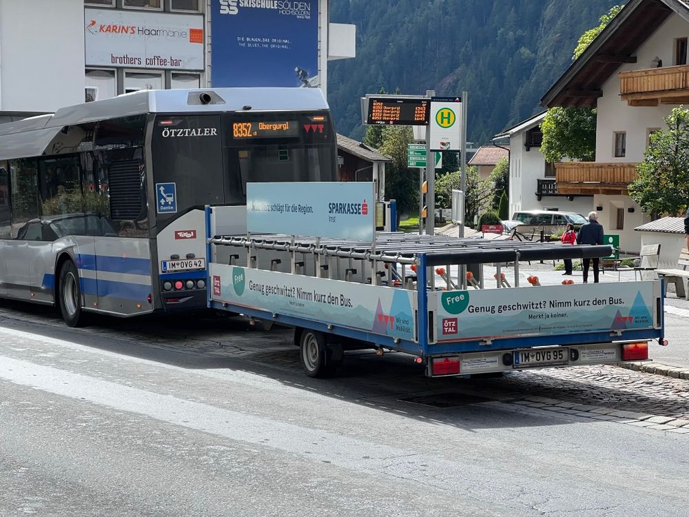 A photo of a bus in the Ötztal Valley in Austria. The bus is towing a trailer a bike racks.