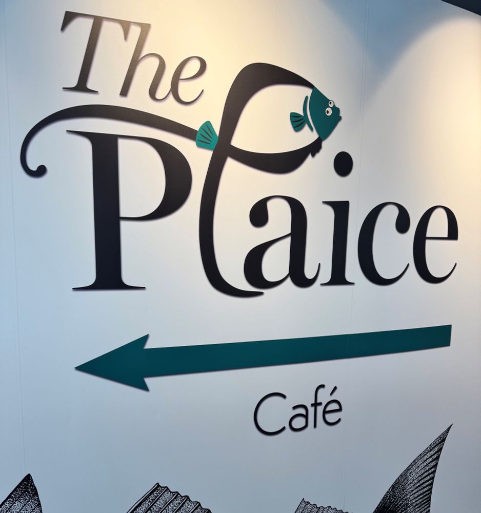 Logo of "The Plaice Café" featuring stylized text and a graphic of a fish, with an arrow pointing left.