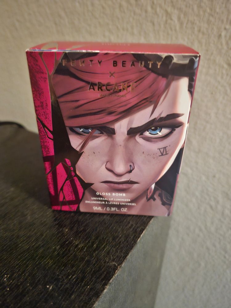 Front of the box of the Vi Fenty lip gloss, featuring a close up of Vi's face looking locked in and determined 