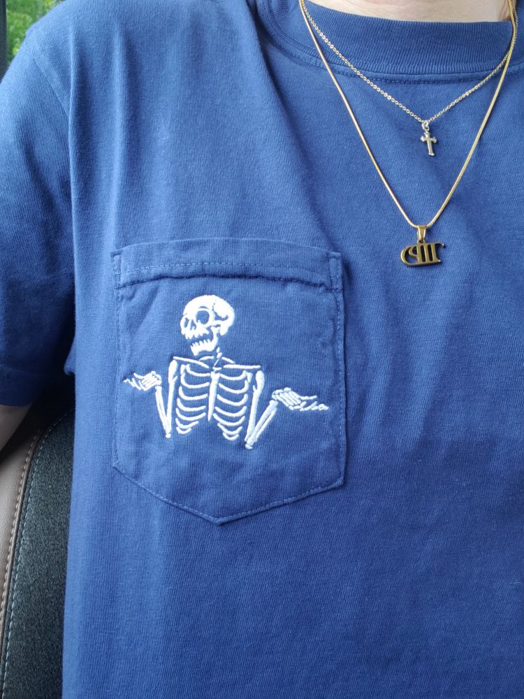 A blue t shirt with a pocket
On the pocket is a white skeleton with his hands face up expressing "who knows"