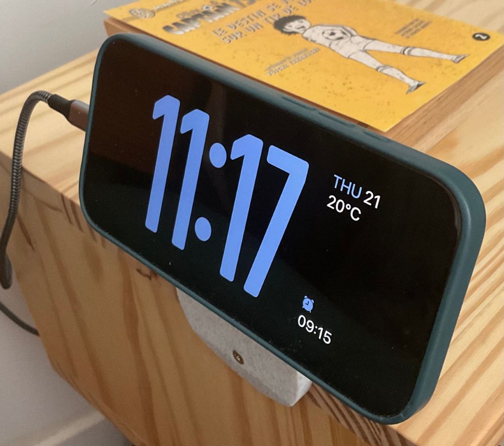 Slanted Magnetic phone holder screwed onto the edge of a pine nightstand with a phone attached to it.