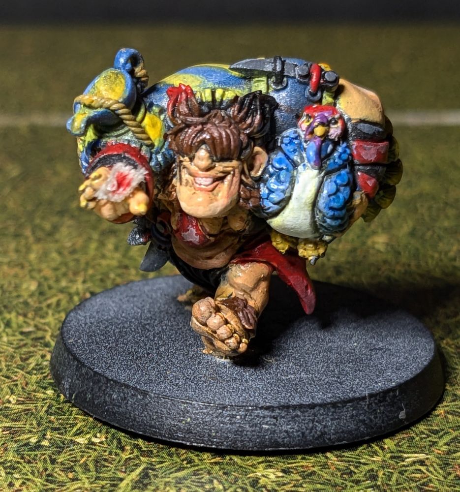 Painted miniature of a halfling by Greebo Games. She is charging forward, a turkey sling under one arm like an American football, and a gravy boat strapped to her other shoulder. Her right arm is sticking out for a stiff arm, and there's a bloody bandage on one of the fingers (it broke off when she fell outside, oops).