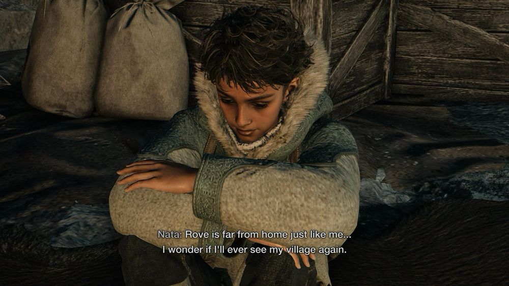 A young boy dressed in winter clothes, sitting with his knees to his chest and his arms crossed on them, a sad and pensive look on his face. Caption reads: “Rove is far from home just like me…I wonder if I’ll ever see my village again.”