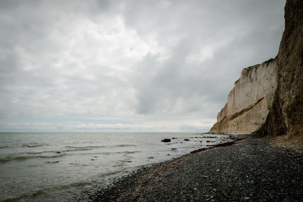 Ostseeufer, Møns Klint. Ein sanftes Meer, steiniger Strand. Rechts Kreidefelsen.