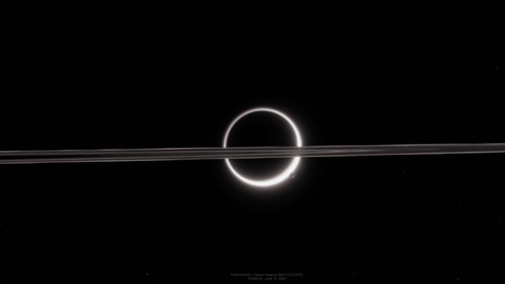mighty Titan is backlit by the sun, causing light to be dispersed around the back of the moon and creating a ring of light that is strongly visible. Saturn’s rings take the foreground, crossing almost directly in front of Titan. On the moon’s lower right limb, Enceladus glows lightly.