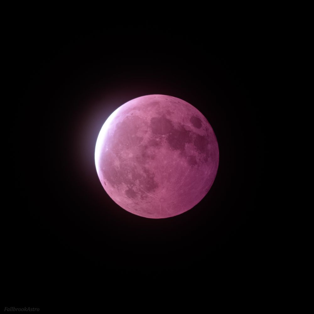 The moon glows red due to every sunset on earth being projected onto it as it passes through our shadow. A sliver of raw sunlight shows on the top left.