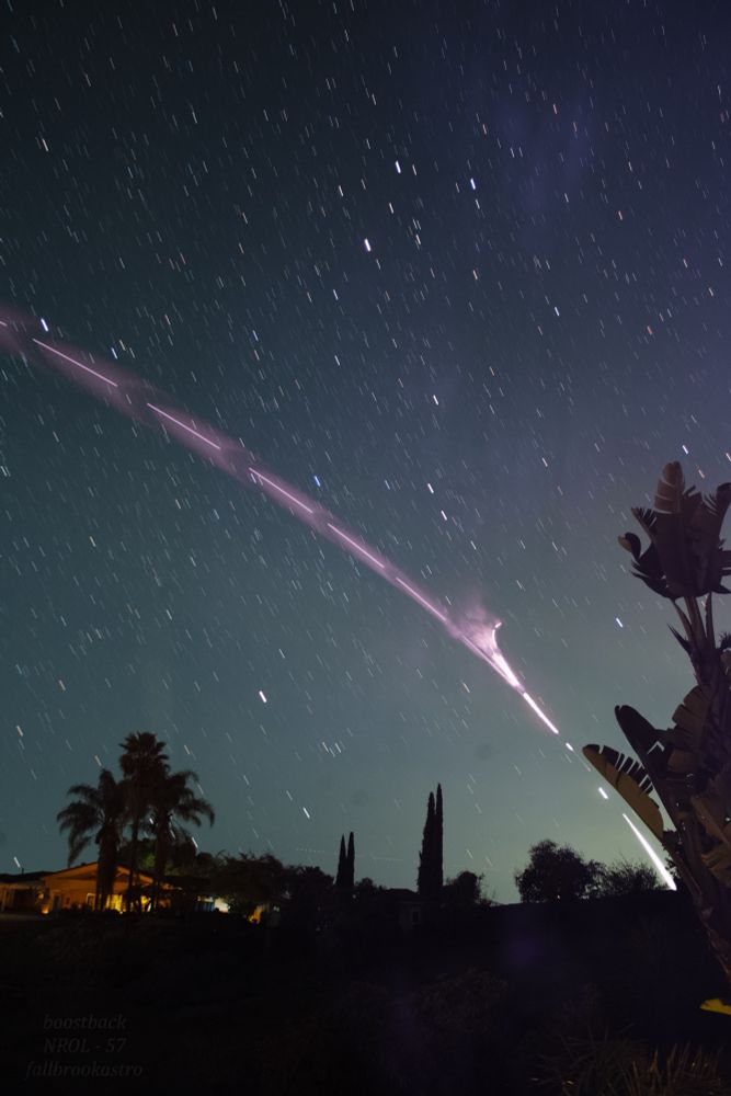 A rocket’s bright engine plume streaks across the night sky, revealing clouds of exhaust interacting with itself, while stars trail slightly in the background.