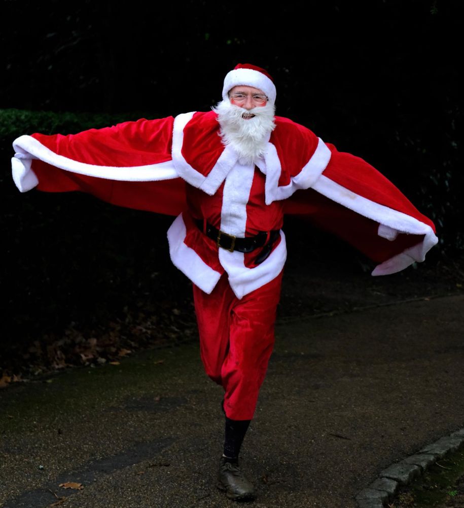 A photograph of a man in a fancy Father Christmas outfit. He has his arms out and a red cloak flowing behind him as he runs towards the camera.